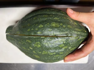 追熟を終え、包丁を入れる前のロロンかぼちゃ（濃い緑にまだらの斑が入るラグビーボール形）